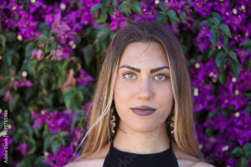 Portrait of a young woman  beautiful  blonde  green eyes  looking at the camera with tender and relaxed attitude with a background of purple bougainvillea. Conceptual looks  eyes  purity  youth.