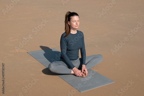 Young woman practicing yoga on mat in lotus position on sandy beach