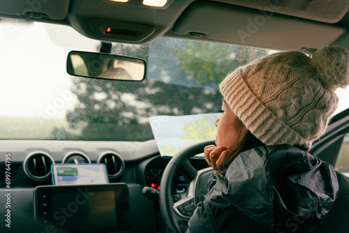 Latin woman leaning on the steering wheel while checking her cell phone and a map to check the route to follow on her trip through Ireland