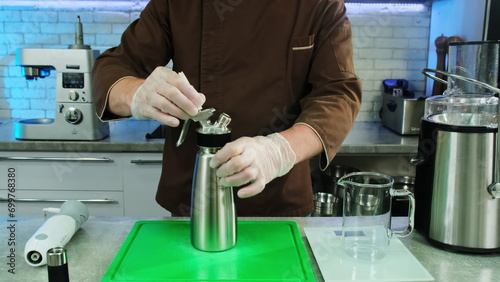 Quadro su tela Chef in uniform screws lid of whipping siphon at table closeup