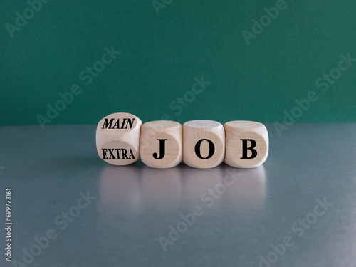 Extra or main job symbol. Turned a wooden cube and changes concept words Extra job to Main job. Beautiful green background, grey table, copy space. Business extra or main job concept. photo