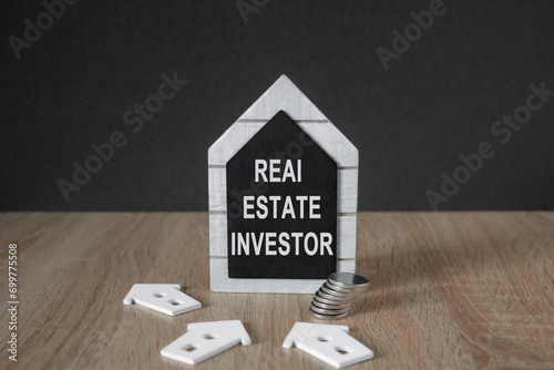 Real estate investor symbol. Black board in the shape of a house with words real estate investor near miniature house. Beautiful wooden table, black backgroundBusiness and real estate investor concept photo