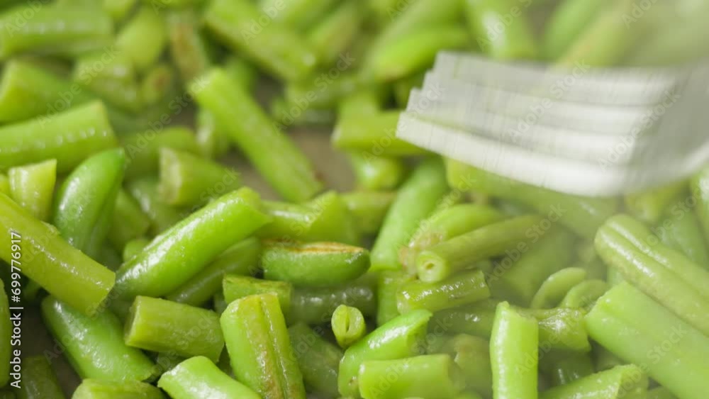 stainless steel fork stirring frying green beans on skillet, full-frame closeup view with selective focus. stainless steel fork stirring frying green beans on skillet, full-frame closeup view with selective focus.