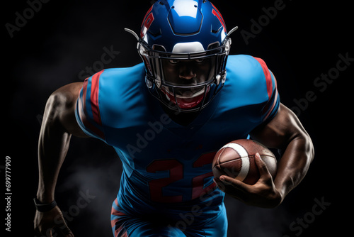 Portrait of American football player running with the ball. Muscular African American athlete in a blue and red uniform with an ovoid ball in a dynamic pose. Isolated on black background.