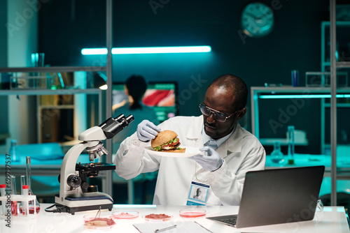Εκτύπωση καμβά African american scientist examining hamburger with lab-grown meat sitting at hi