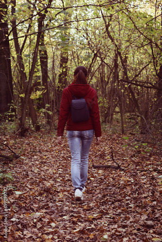 woman with backpack in red jacket walking in autumn woods. Female explorer walking in forest