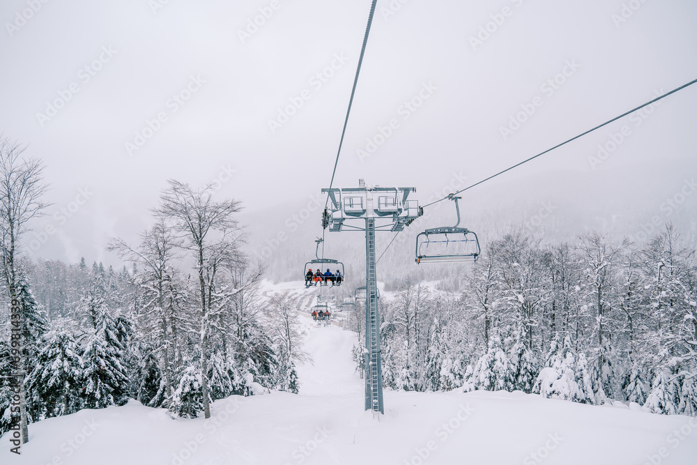 Skiers ride on four-seater chairlifts above snow-covered trees