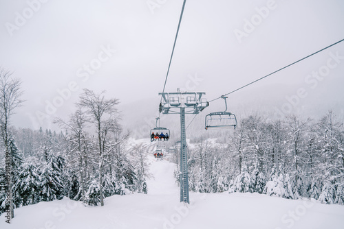 Skiers ride on four-seater chairlifts above snow-covered trees