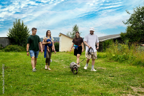Young people with baby and dog walk through village on summer day. © grigvovan