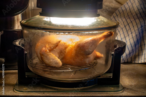 A chicken cooking in a halogen oven on a kitchen worktop