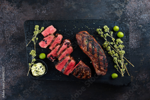 Barbecue dry aged angus roast beef steak with herb butter and dried oregano served as top view on a rustic charred cutting board with copy space photo