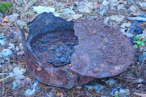 one old rusty broken iron brown barrel with a lid stands on the ground on the street