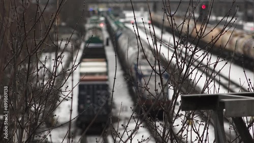 a train moving through a railroad yard in winter is seen through the branches of bare trees, focusing on the approach of the lead locomotive, signaling and transit in the cold season. photo