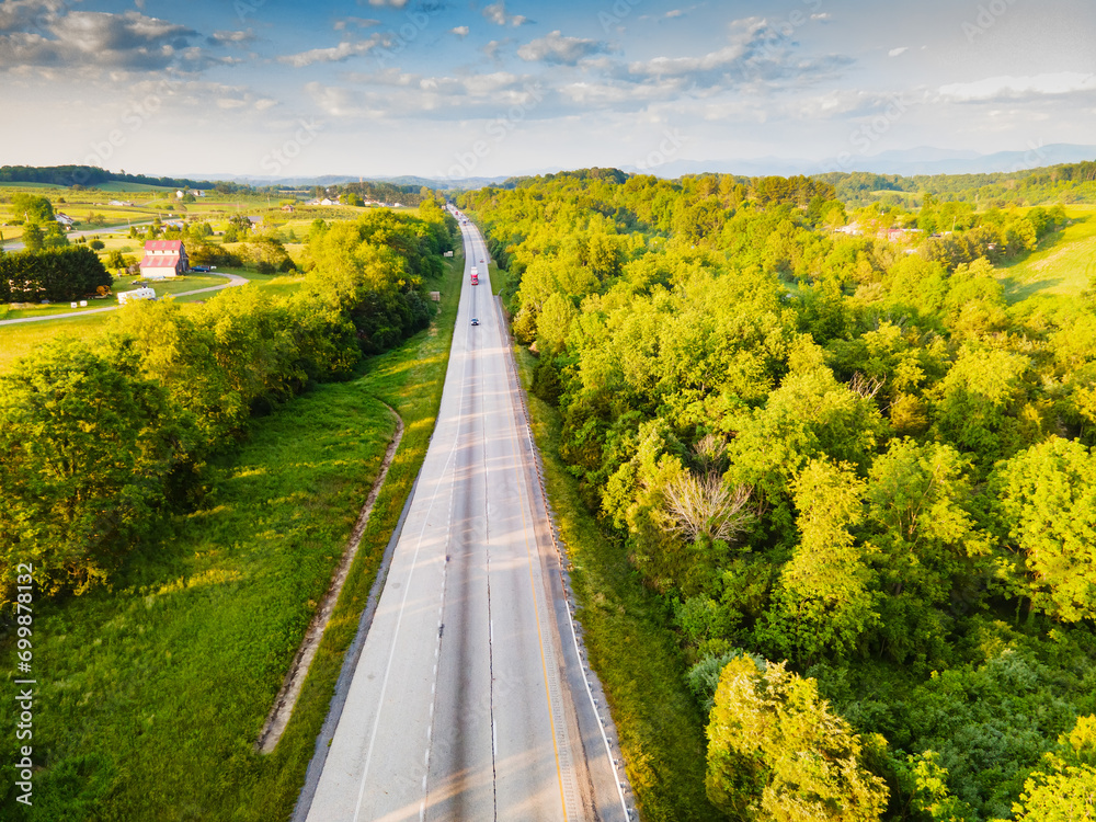 Naklejka premium Aerial view of the road. Top view from drone of road in woods. Beautiful landscape with roadway, forest, houses, green meadows.