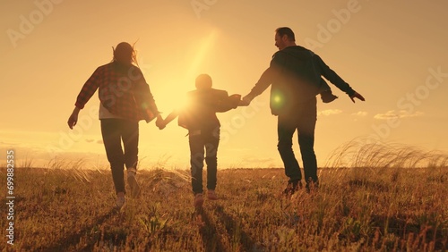 Parents, daughter are run at sunset, dream is to fly like an airplane. Family playing in park, child mom dad run. Happy family running in park at sunset, holding hands, dream flight concept. Teamwork