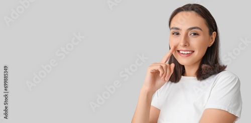 Young woman pointing at her nose on grey background with space for text photo