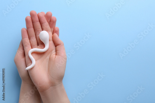 Reproductive medicine. Woman holding figure of sperm cell on light blue background, top view with space for text photo