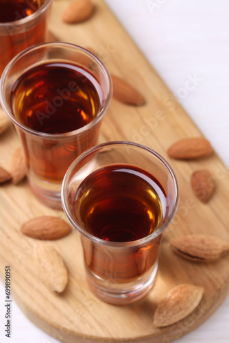 Shot glasses with tasty amaretto liqueur and almonds on white wooden table, closeup