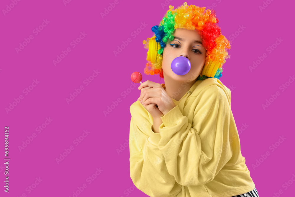 Trendy girl with lollipop blowing bubble gum on purple background