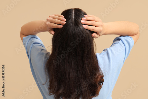 Young woman with dandruff on beige background, back view