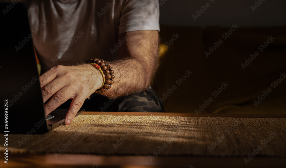 Closeup of arm of adult man using laptop with bracelets on wrist - obrazy, fototapety, plakaty 