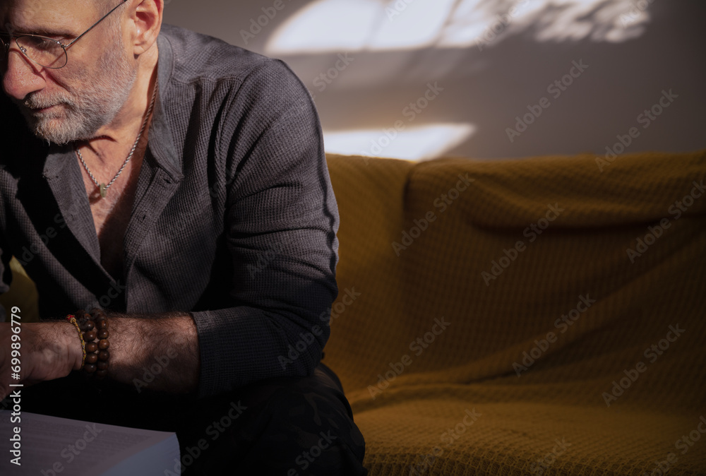Obraz premium Adult man reading on sofa with bracelets on wrist and necklace on neck