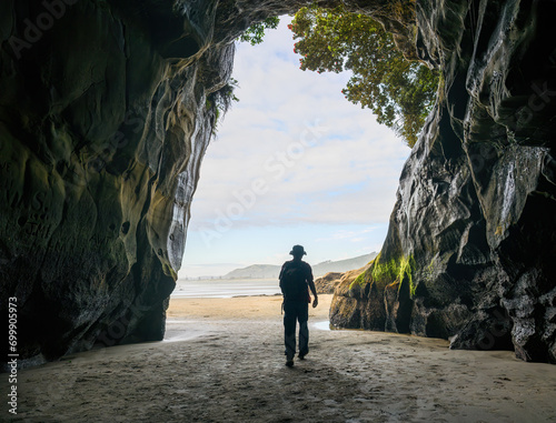 Entrance to Muriwai cave with a silhouette man walking. Muriwai Beach in summer. Auckland. photo