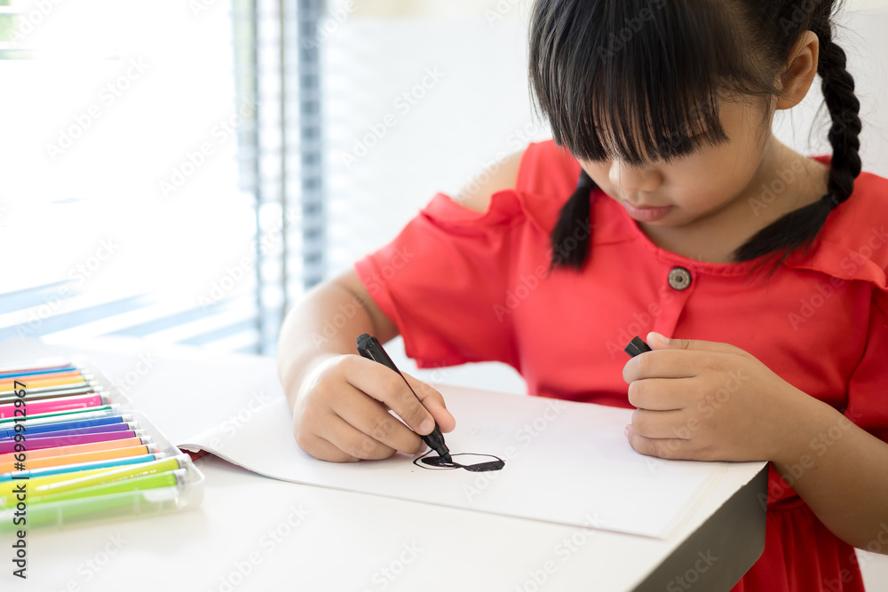 Asian little girl drawing with colorful pens on the table at home Asian little girl drawing with colorful pens on the table at home