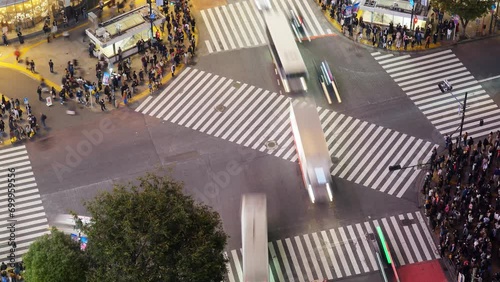 Cars pass by, and the intersection is filled with people crossing street, time lapse shot from above. Scramble crosswalk at Shibuya in busy evening hour, busy life at modern and big Asian city photo