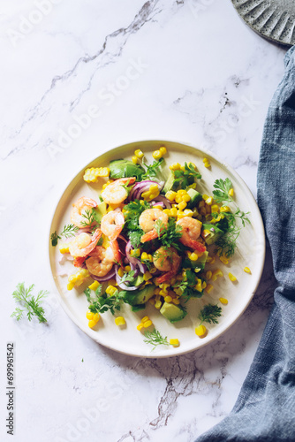 Healthy salad with fresh vegetables - corn, avocado, red onion, shrimp and coriander on a white plate.