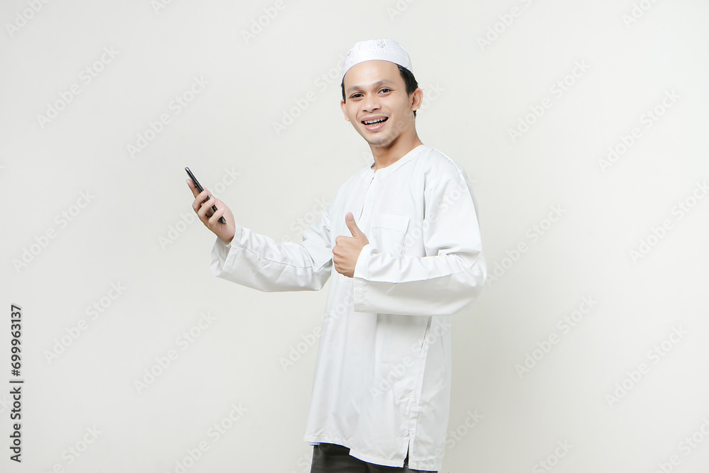 happy muslim man holding mobile phone and give tumb up gesture. People religious Islam lifestyle concept. celebration Ramadan and ied Mubarak. on isolated background. happy muslim man holding mobile phone and give tumb up gesture. People religious Islam lifestyle concept. celebration Ramadan and ied Mubarak. on isolated background.