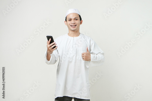 happy muslim man holding mobile phone and give tumb up gesture. People religious Islam lifestyle concept. celebration Ramadan and ied Mubarak. on isolated background.
