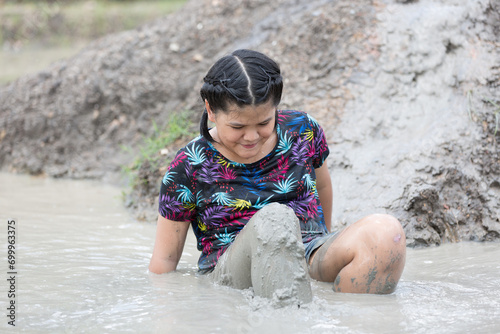 Cheerful little child girl playing on heap of wet mud soil during raining in rainy season. Girl playing in wet mud puddle and dirt in rainy season
