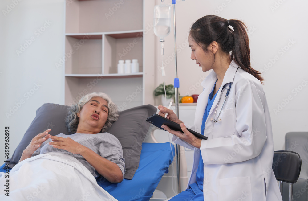 Obraz premium Elderly Asian woman lying in hospital bed looking unwell, with young Asian doctor take a history of illness Health check and encouragement.