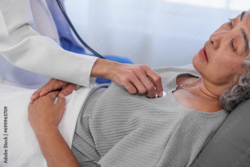 Elderly Asian woman lying in hospital bed looking unwell, with young