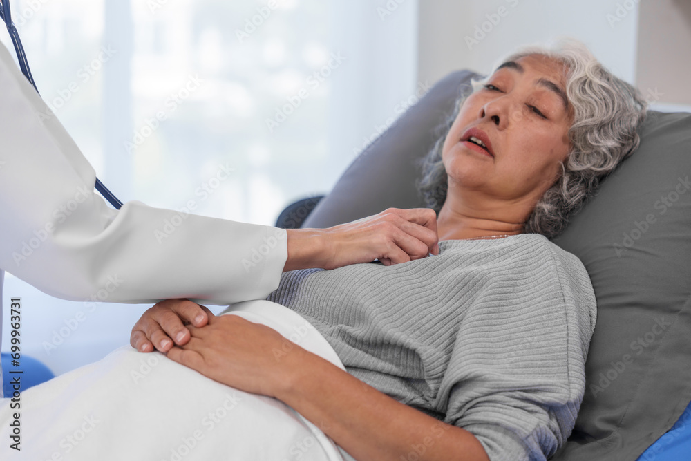 Elderly Asian woman lying in hospital bed looking unwell, with young