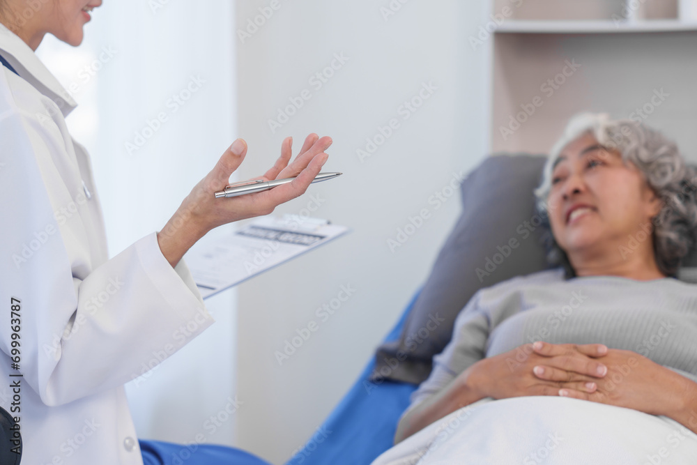 Obraz premium Elderly Asian woman lying in hospital bed looking unwell, with young Asian doctor take a history of illness Health check and encouragement.