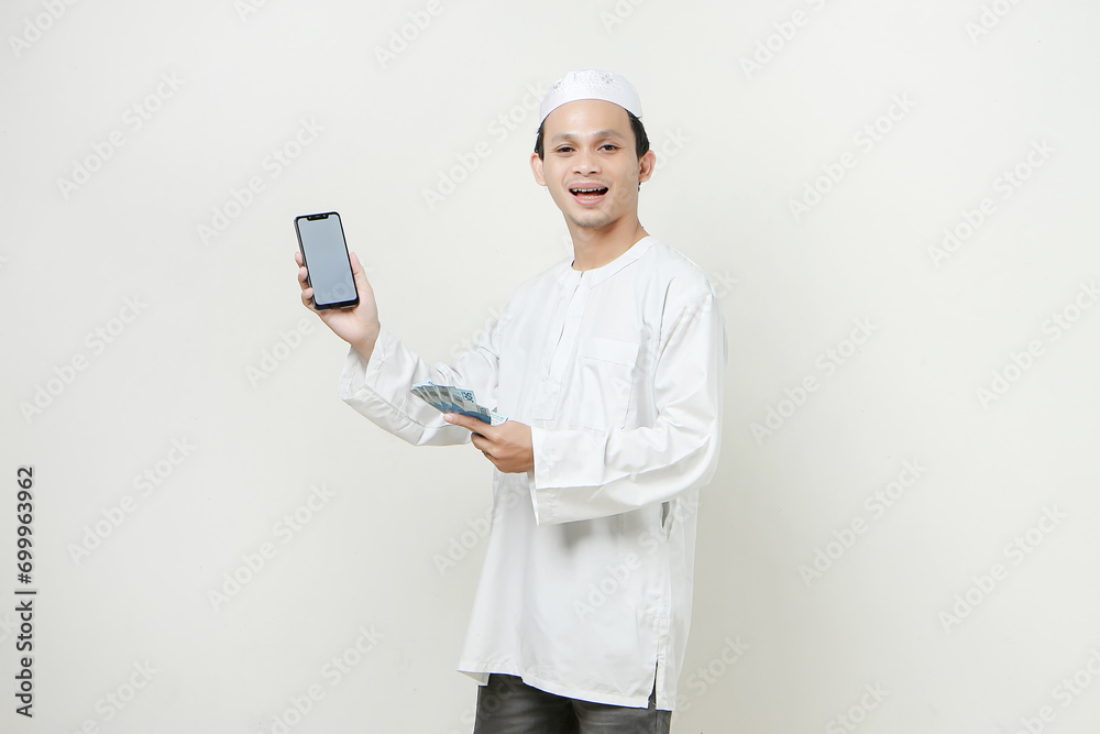 happy muslim man holding money rupiah banknotes and showing mobile phone blank screen. People religious Islam lifestyle concept. celebration Ramadan and ied Mubarak. on isolated background. happy muslim man holding money rupiah banknotes and showing mobile phone blank screen. People religious Islam lifestyle concept. celebration Ramadan and ied Mubarak. on isolated background.