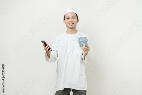 happy muslim man holding money rupiah banknotes and mobile phone. People religious Islam lifestyle concept. celebration Ramadan and ied Mubarak. on isolated background.