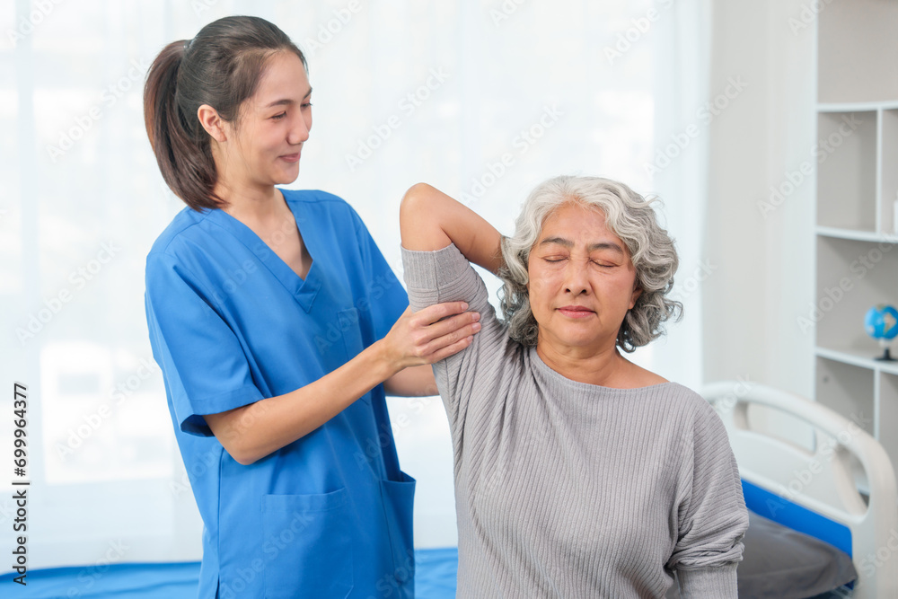 A young Asian nurse is assisting an elderly Asian woman with a grey hair during a physical therapy session. A young Asian nurse is assisting an elderly Asian woman with a grey hair during a physical therapy session.