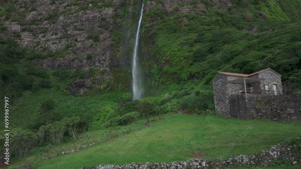 Flying towards cascata do poço do bacalhau waterfall with house at Flores island - Drone shot