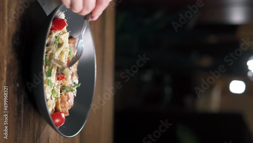 Eating farfalle pasta with chicken, cheese and tomatoes while sitting in a restaurant. Italian pasta concept photo