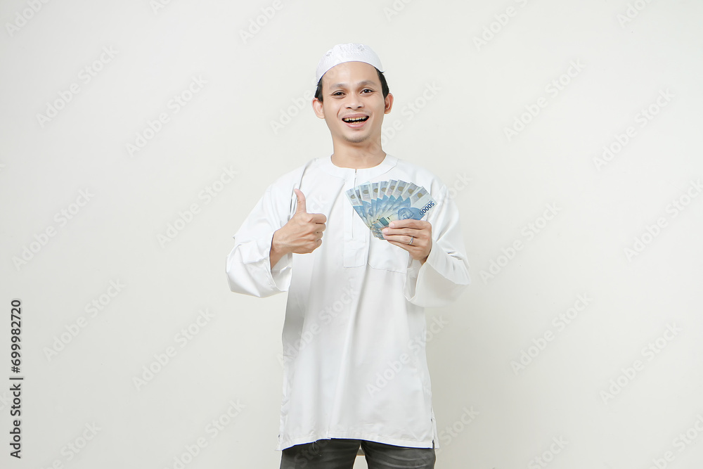 happy muslim man holding money rupiah banknotes and give thumb up. People religious Islam lifestyle concept. celebration Ramadan and ied Mubarak. on isolated background. happy muslim man holding money rupiah banknotes and give thumb up. People religious Islam lifestyle concept. celebration Ramadan and ied Mubarak. on isolated background.