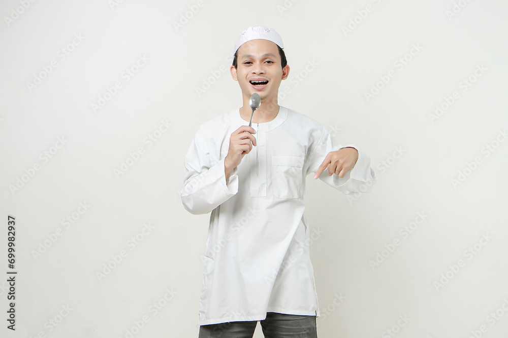 muslim man holding spoon and give pointing finger gesture. People religious Islam lifestyle concept. celebration Ramadan and ied Mubarak. on isolated background. muslim man holding spoon and give pointing finger gesture. People religious Islam lifestyle concept. celebration Ramadan and ied Mubarak. on isolated background.