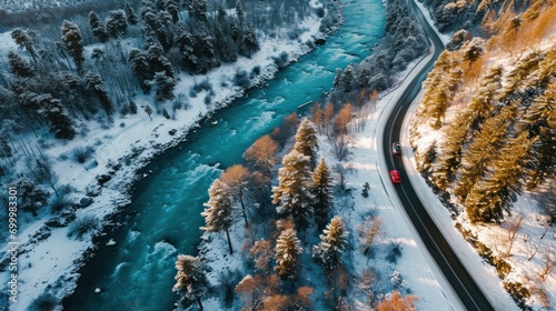 Aerial top view of winter snowy road with red cars over blue river.