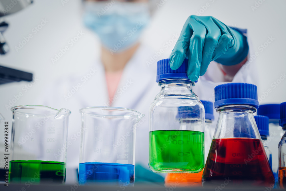 A scientist examines samples with a microscope in a laboratory with test tubes filled with colorful liquids in the background. A scientist examines samples with a microscope in a laboratory with test tubes filled with colorful liquids in the background.