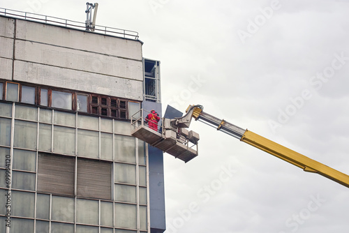 Workers in boom lift repair and install LED billboard on building. Man in lifting paltform work at height, installing LED display screen on building facade photo