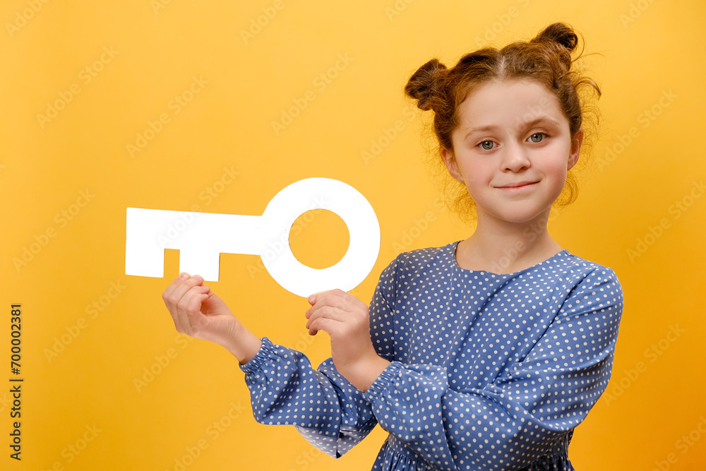 Portrait of beautiful smiling preteen girl kid holding white paper key, happy looking at camera, posing isolated over plain yellow color background wall in studio. Concept of real estate services Portrait of beautiful smiling preteen girl kid holding white paper key, happy looking at camera, posing isolated over plain yellow color background wall in studio. Concept of real estate services