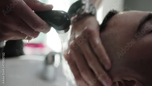 A master in a barbershop washes the hair of a male client with shampoo and water after a haircut. Modern and fashionable haircut. Slow motion photo