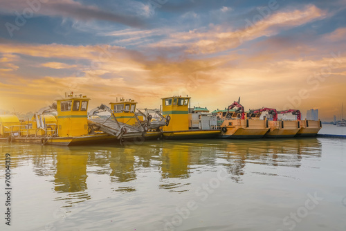 Small several row of ships with a claw manipulator hand parked at the port pier at sunset sky photo